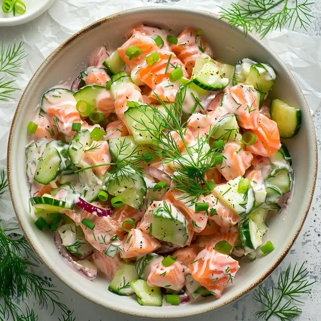Overhead shot of creamy salmon cucumber salad served in a white bowl, showing flaked salmon, cucumber, dill, and dressing.