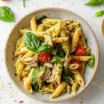 Flat lay of a clean recipe card for tuna pesto pasta, showing ingredients and cooking steps alongside a bowl of penne pasta with tuna, pesto, spinach, and cherry tomatoes.
