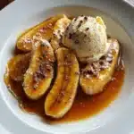 Overhead view of Bananas Foster recipe with halved bananas in caramel sauce and a scoop of vanilla ice cream